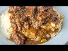 a white plate topped with meat and gravy covered in gravy on top of mashed potatoes