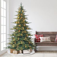 a small christmas tree sitting next to a wooden bench in a room with white walls