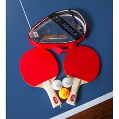 two ping pong paddles and three balls in a red case on a blue surface