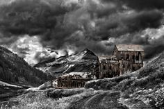 black and white photograph of an old abandoned building in the mountains with storm clouds overhead