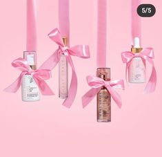 three bottles with pink ribbons hanging from them on a pink background next to each other