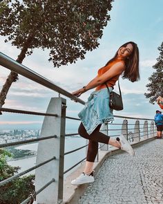 a woman leaning on a railing with her hand in her pocket and looking at the camera