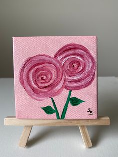 a pink painting on a wooden easel with three flowers painted on the top and bottom