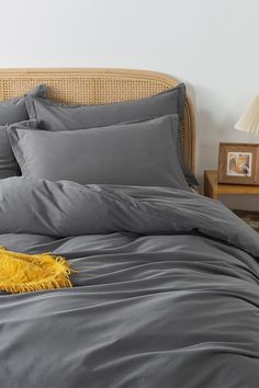 a bed with grey sheets and pillows on it