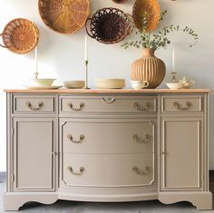 an antique dresser with wicker baskets on the wall above it and plates hanging on the wall behind it