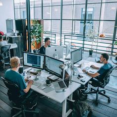 people sitting at desks working on computers in an open room with lots of windows