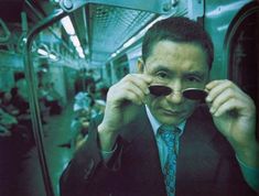 a man in a suit and tie on a subway train holding his sunglasses up to his face