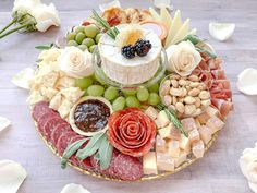 an assortment of cheeses, meats and vegetables on a platter with flowers