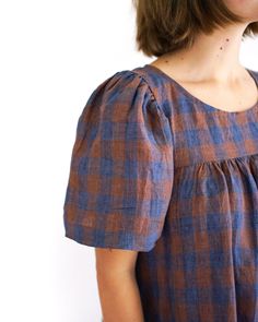 a woman wearing a brown and blue checkered dress standing in front of a white wall