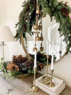 a christmas wreath with pine cones and candles on a table next to a candle holder