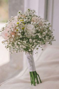 a bridal bouquet with white and pink flowers on a bed in front of a window