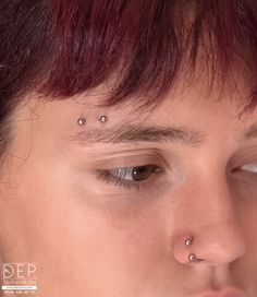 a close up of a person with piercings on their nose and forehead, looking at the camera