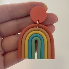 a hand holding a pair of rainbow shaped earrings