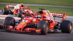 two red racing cars driving on a race track with grass in the backgroud