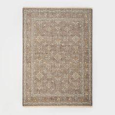 a beige rug with an intricate design on the top and bottom, in front of a white wall