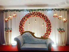 a couch sitting in front of a white curtain with red flowers on it and lights hanging from the ceiling