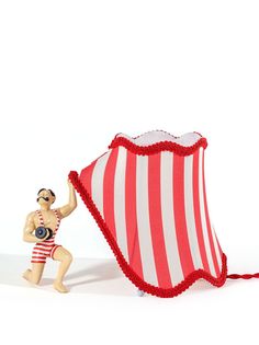 a figurine is holding up a red and white striped lamp shade that looks like a man