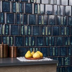 three pears on a plate in front of a blue tiled wall with copper accents