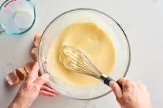 two hands whisk batter into a glass bowl with eggs on the counter next to it