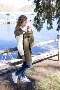 a woman holding a baby on top of a wooden fence next to the water with boats in the background