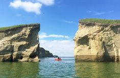 two large rocks sticking out of the water with people in kayaks paddling between them