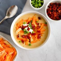 two bowls of soup with carrots, bacon and green onions next to spoons