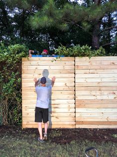 a man standing in front of a wooden fence with his hands up to the side