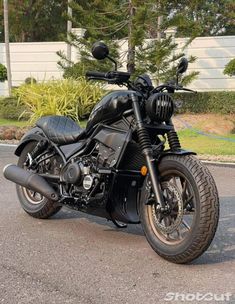 a black motorcycle parked on the street in front of some bushes and trees with no one around it