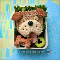 a lunch box with a dog made out of bread and vegetables in it's mouth