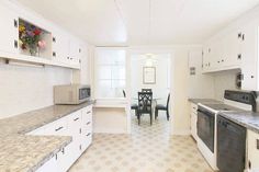 a kitchen with white cabinets and marble counter tops, along with a dining room table