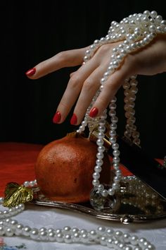 a woman's hand reaching for a piece of fruit on a table with pearls