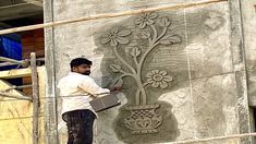 a man standing on a scaffold in front of a wall with a flower design