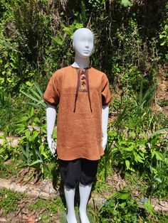 This tunic is what we call our "medieval T-shirt". It is a fairly loose fitting tunic, a little shorter than our Viking style tunics with small side slits instead of the side gores and with shorter sleeves, perfect for those hot weather events or even just to wear as a regular shirt! This one is made of terra cotta orange linen with brown, orange, and metallic gold ribbon trim at the neck and ends of sleeves. It is a comfy pullover style with metal eyelets and a cotton ribbon that laces up the neck. Machine washable and dry-able. Iron as needed. This tunic is a child size 11/12. Will fit chest  26"-28"  (loose fit), and length from top of shoulder to hem is 27". Sleeves are 7" long. Coos Bay, Medieval Style, Cotton Ribbon, Viking Style, Medieval Fashion, Gold Ribbon, Gold Ribbons, Ribbon Trim, Brown Orange