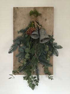 a christmas wreath with bells and greenery hanging on a wooden board against a white wall