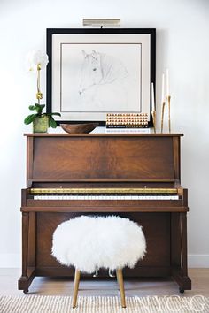 a piano with a white fur stool in front of it and a painting on the wall