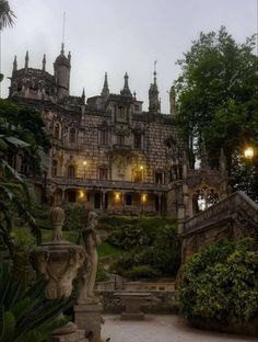 an old castle with statues in front of it at night time, surrounded by greenery and trees