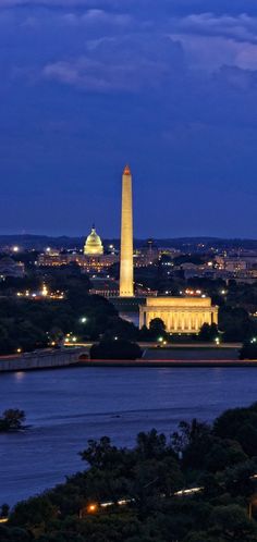 the washington monument is lit up at night with lights on it's sides and trees in the foreground