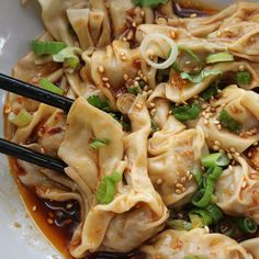 a white plate topped with dumplings covered in sauce and veggies next to black chopsticks