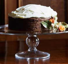 a chocolate cake with white frosting and orange flowers on a glass plate sitting on a wooden table