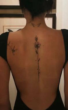 the back of a woman's body with tattoos on it and flowers growing out of her lower back