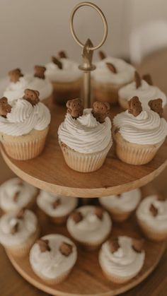 cupcakes with white frosting and brown teddy bears on top are arranged on a three - tiered cake stand