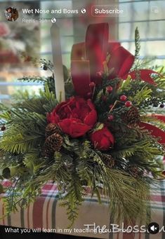 a vase filled with red flowers and greenery on top of a plaid table cloth