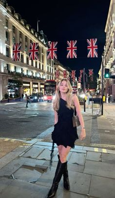 a woman in black dress and boots standing on sidewalk