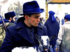 a man in a blue hat and coat holding a goat with other men in the background