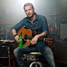 a man sitting in a chair holding a guitar and a bottle with a light shining on him