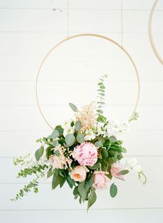 a floral arrangement hanging from a hoop on the wall with greenery and flowers in it