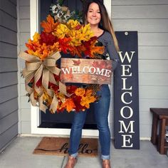 a woman standing in front of a door holding a welcome sign with fall leaves on it