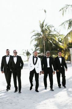 four men in tuxedos walking on the beach