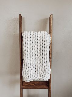 a white knitted blanket sitting on top of a wooden chair next to a wall