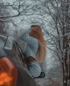 a woman leaning on the back of a car in front of some snow covered trees